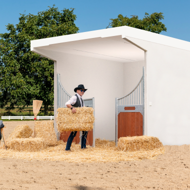 Moderne weiße Pferdebox mit einem Mann, der Heu hineinbringt, zeigt eine funktionale und gut gestaltete Stalllösung für Pferde.