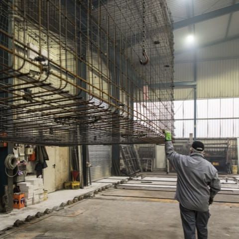 Hal met stalen wapening voor betonproducten. Arbeider met opgeheven hand inspecteert constructie.