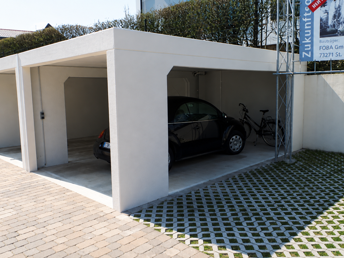 Rijhuisgarage met drie parkeerplaatsen, een auto en een fiets erin. Geplaveide binnenplaats ervoor.