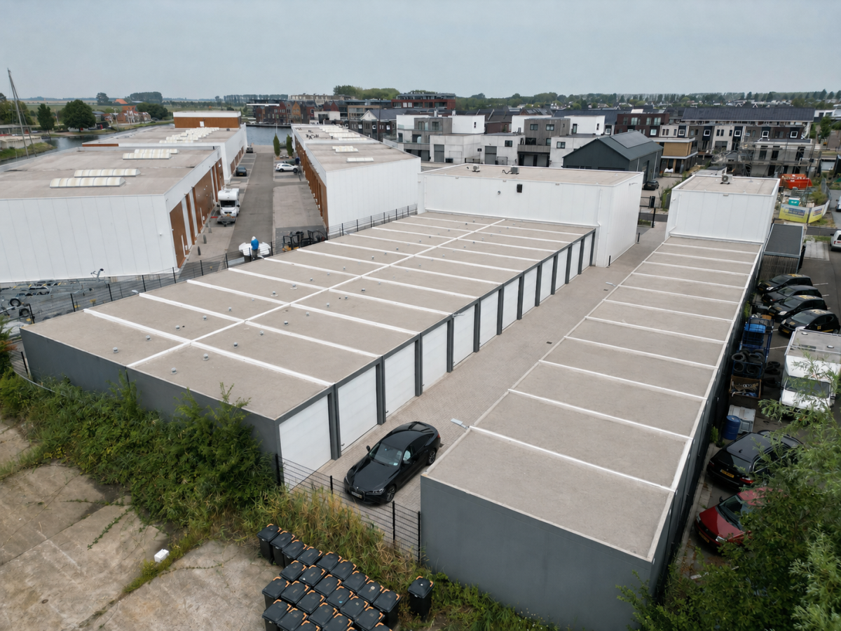 Laagbouw met garagedeuren en platte daken, omgeven door groen en straten.