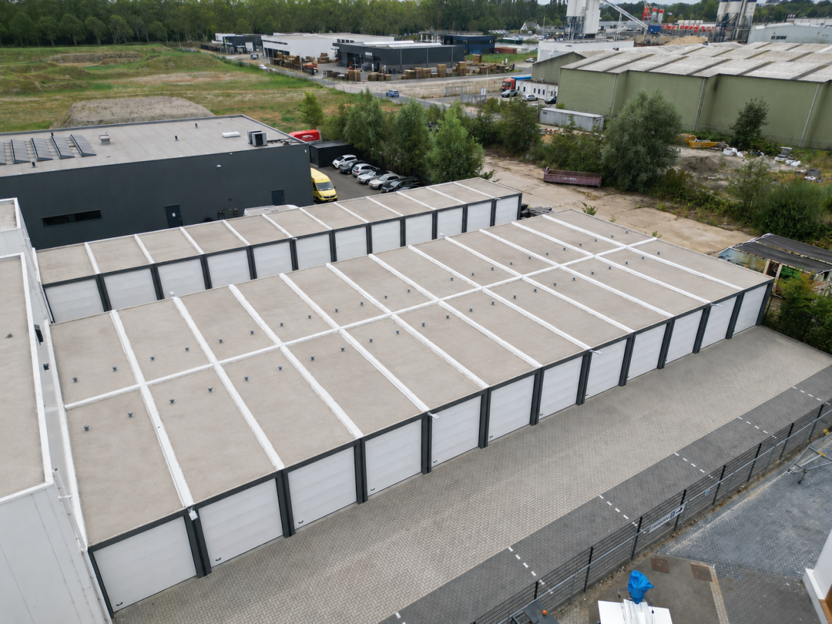 Luchtopname van een industriegebied met lange, platte opslaghallen met witte roldeuren en aangrenzende gebouwen.