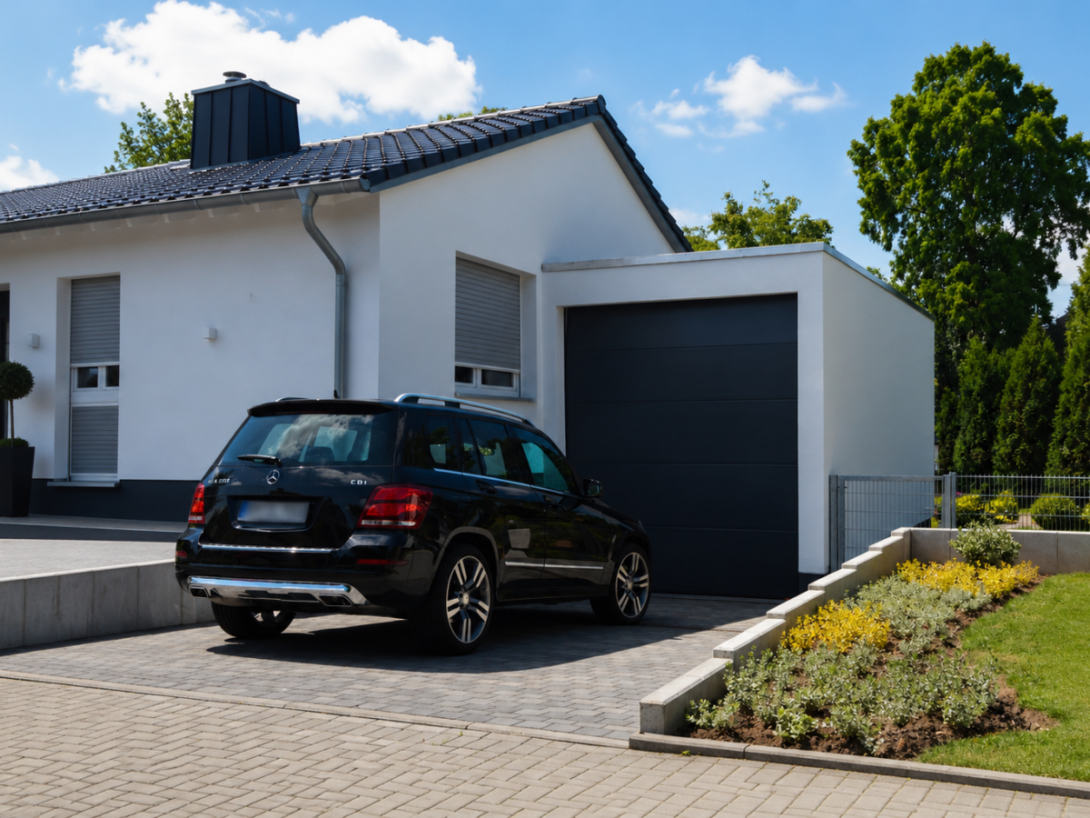 Modern woonhuis met zwarte SUV op bestrate oprit. Verzorgde tuin.