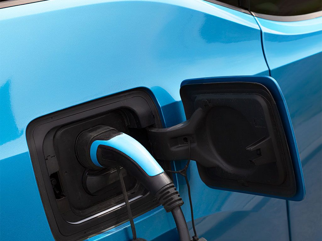 Lichtblauwe elektrische auto wordt opgeladen aan een laadpaal. Kabel en stekker zichtbaar.