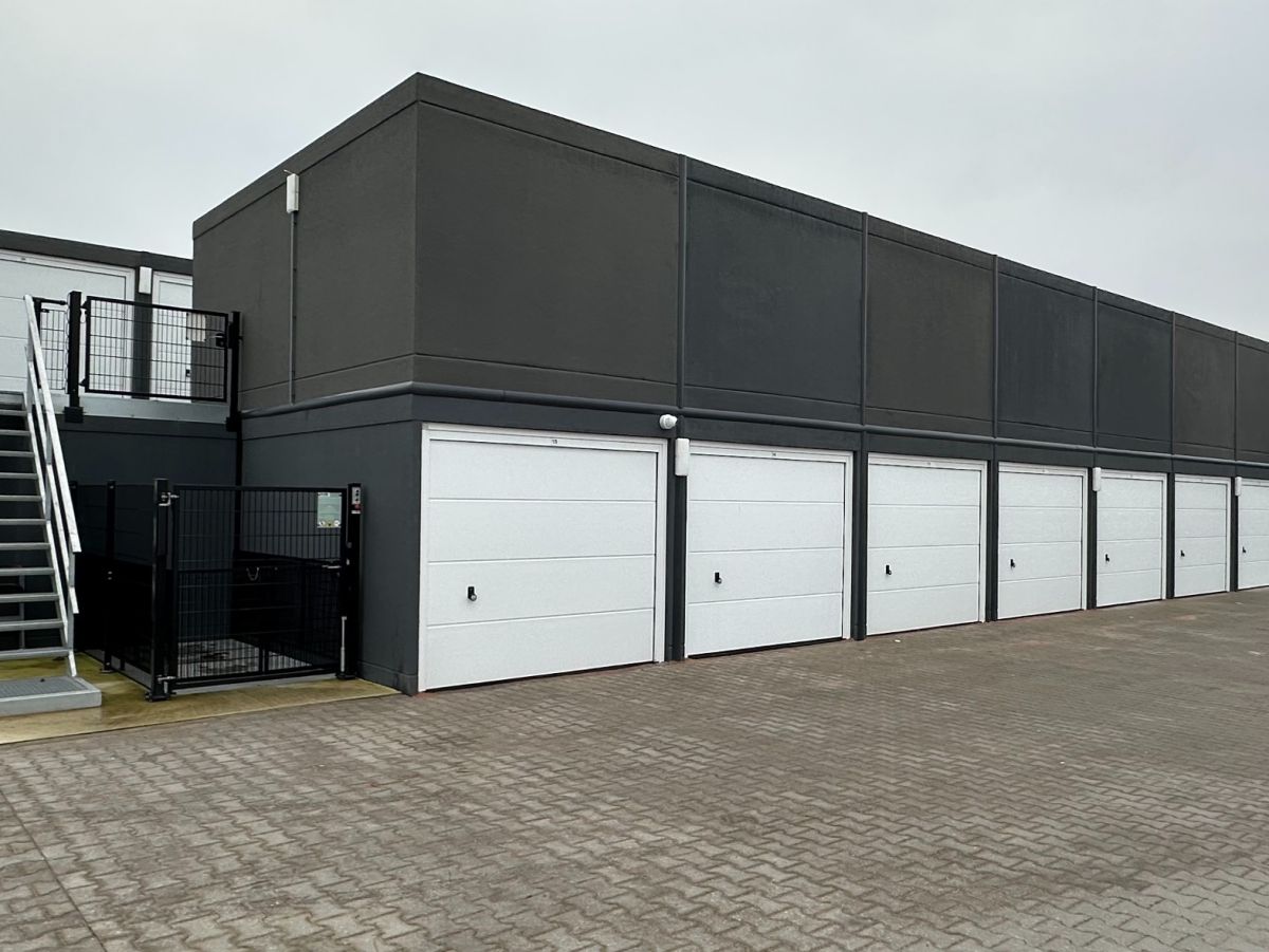 Eén verdieping garagegebouw met zes witte garagedeuren en trap naar het dak.