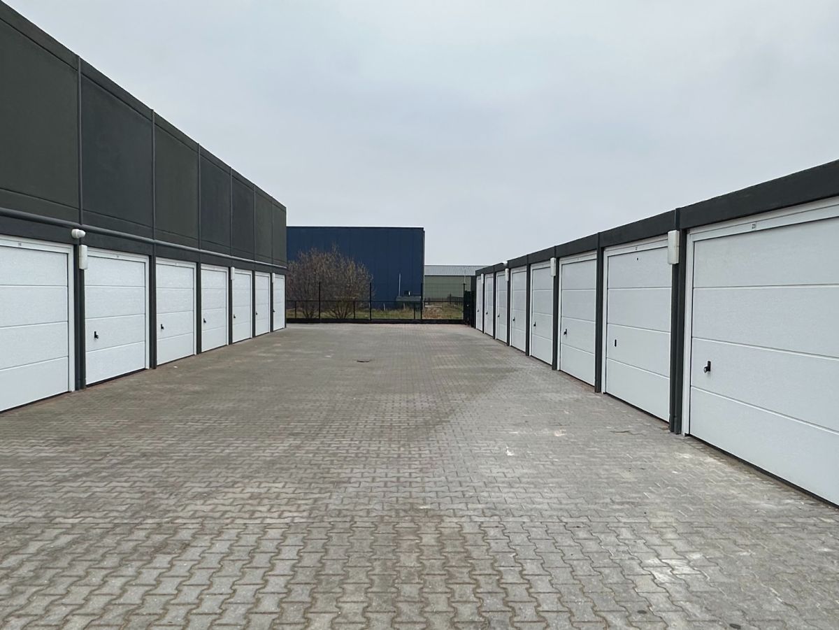 Rij garages met witte deuren voor een geplaveide binnenplaats onder een grijze lucht.