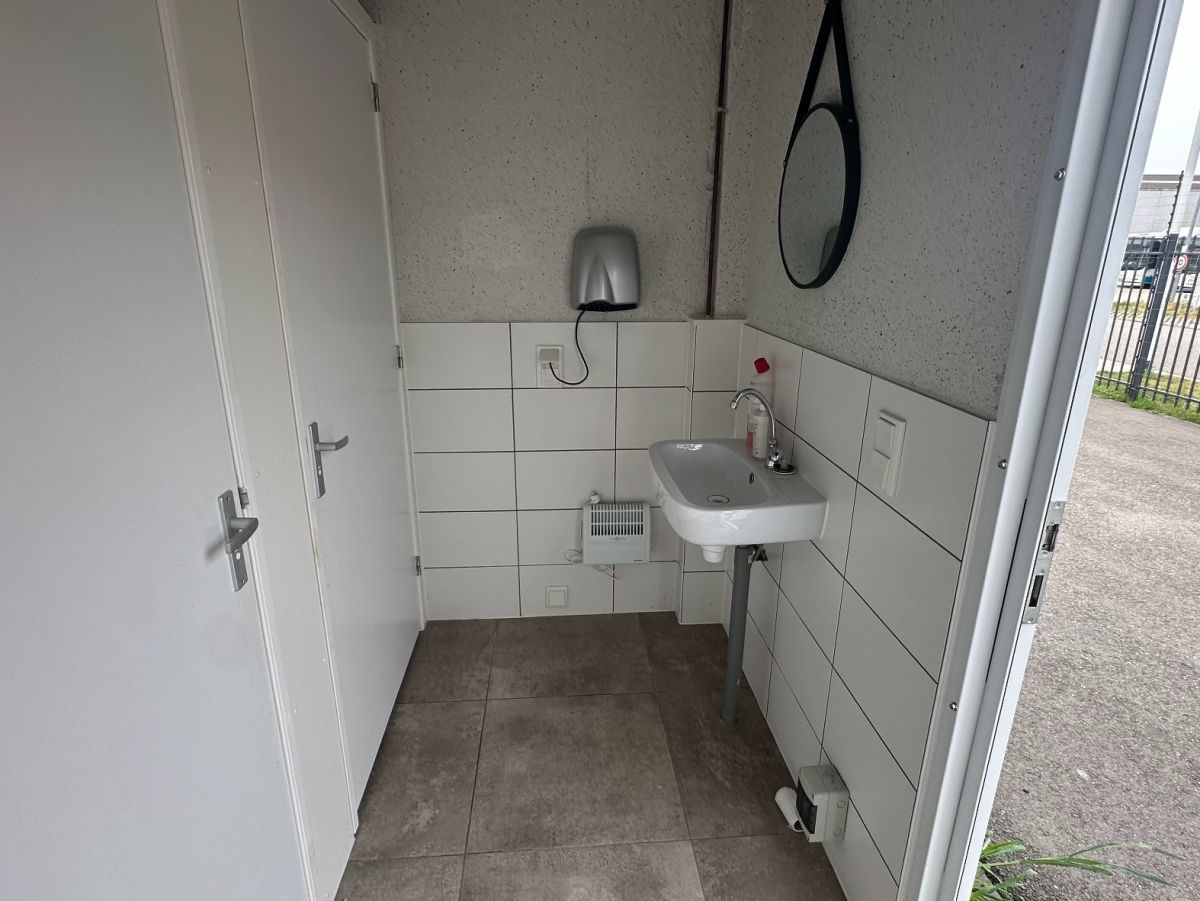 Eenvoudige wasruimte met wastafel, spiegel en deur. Tegelwanden en -vloer.
