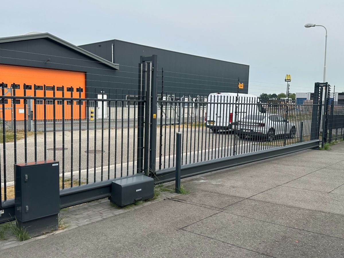 Inritpoort naar een industriegebied. Donker metalen hek met schuifpoort en beveiligingshek.