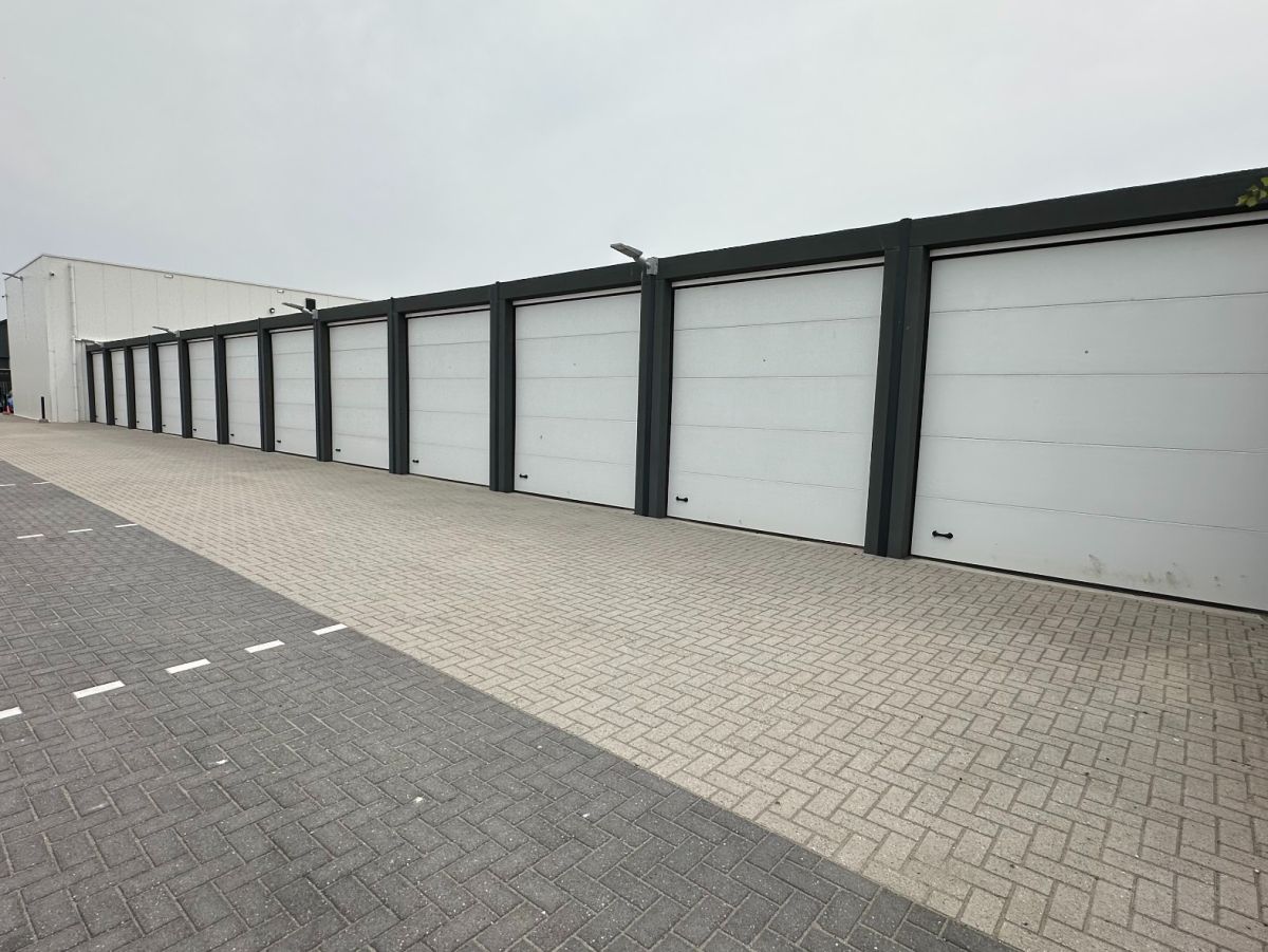 Rij witte garagedeuren met grijze frames aan een bestraatte weg.