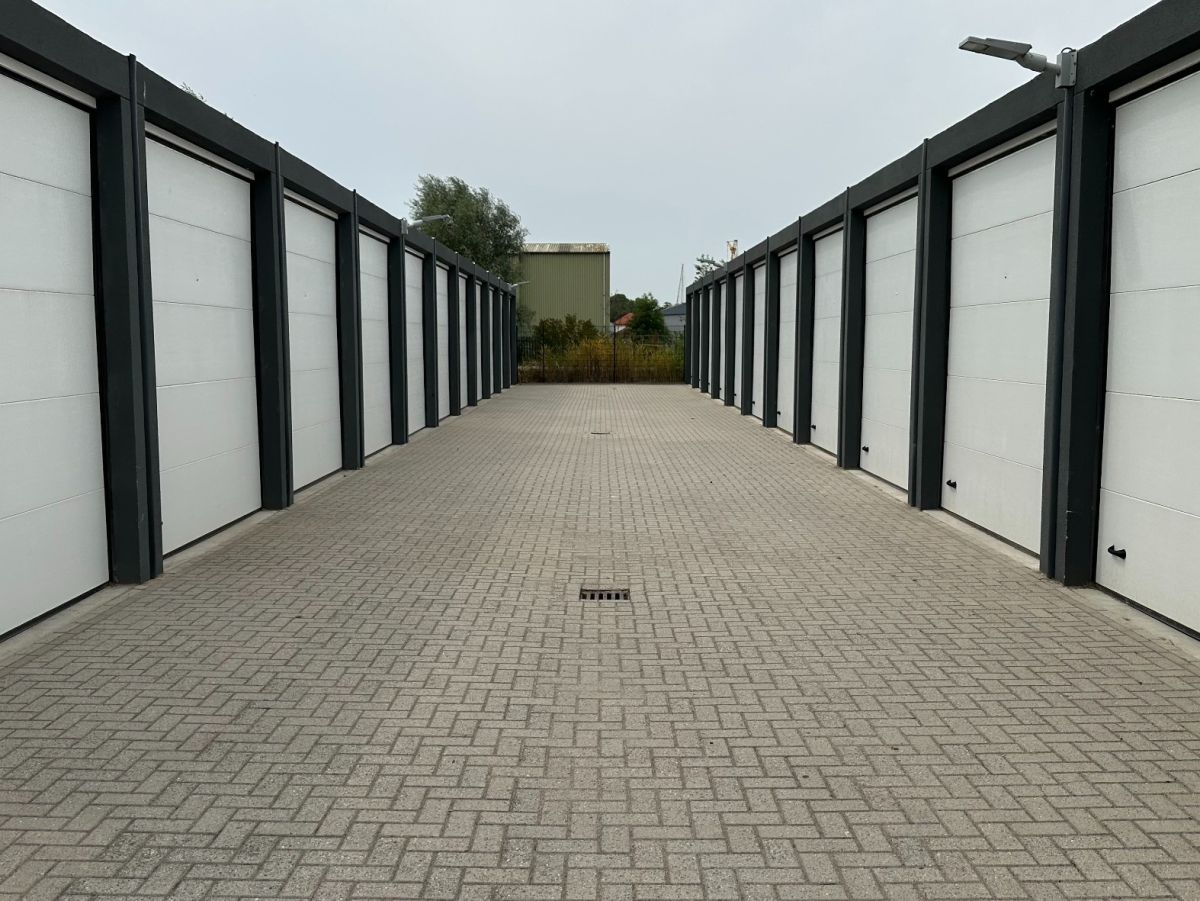 Rij witte garagedeuren met een grijs bestraat pad ervoor.