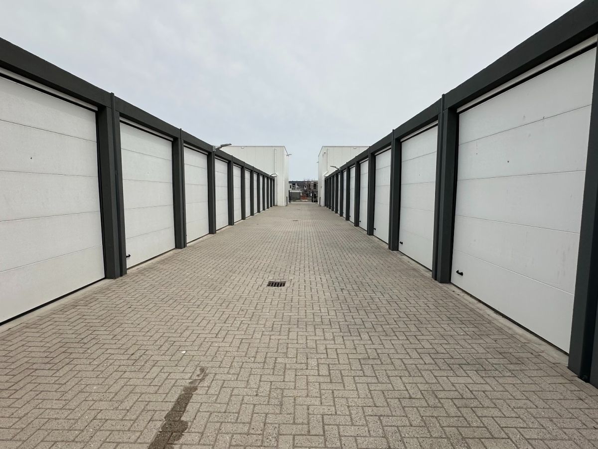 Rij witte garagedeuren met grijze frames, geplaveide weg ertussen, bewolkte lucht.