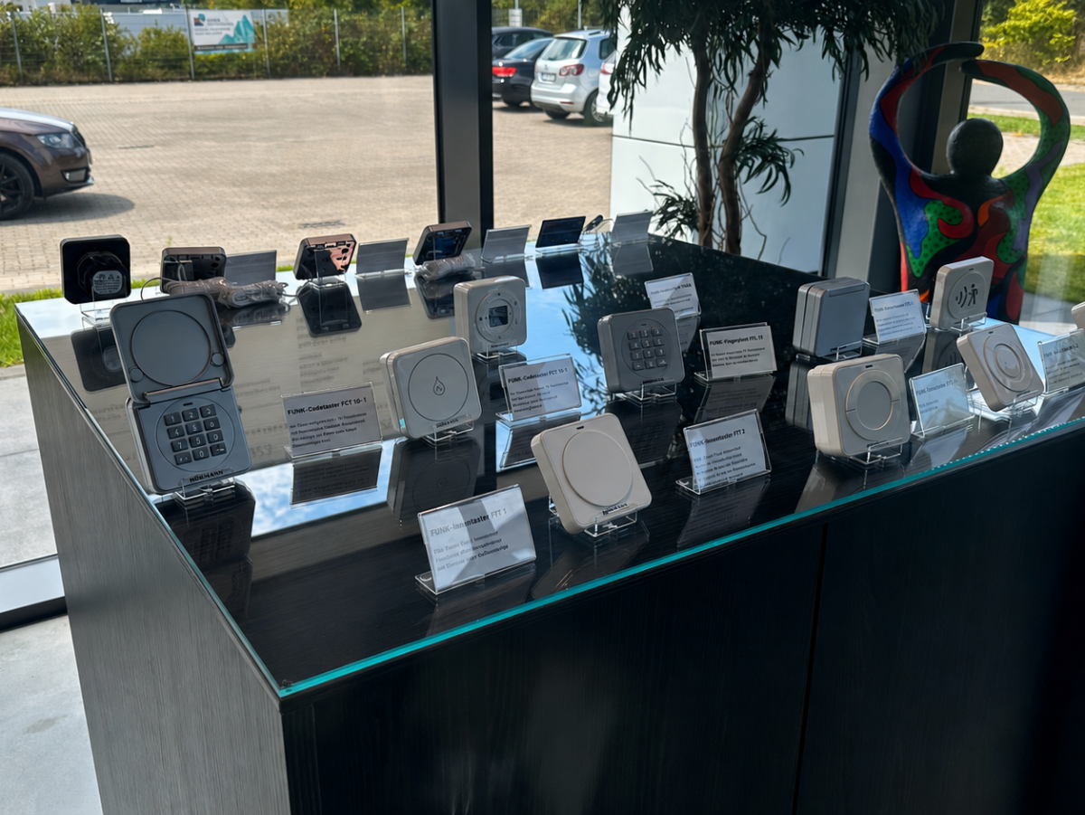 Presentatie van deurspreekinstallaties in een glazen vitrine. Op de achtergrond auto's en grasvelden.