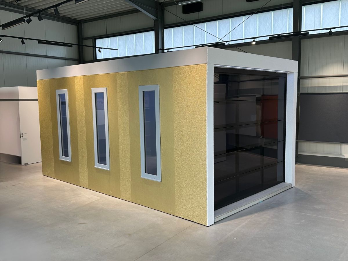 Gele prototype van een geluidsdichte cabine met smalle ramen in een magazijnruimte.