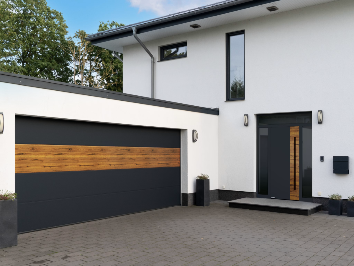Modern huis met witte gevel, donker zadeldak en grijze garage. Voor het huis plantenbakken en bestrate binnenplaats.