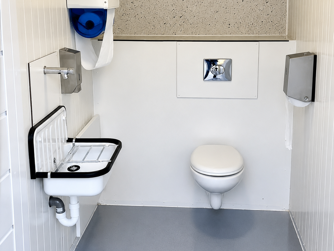 Toegankelijk toilet met wandcloset, inklapbare wastafel en handdoekdispenser.