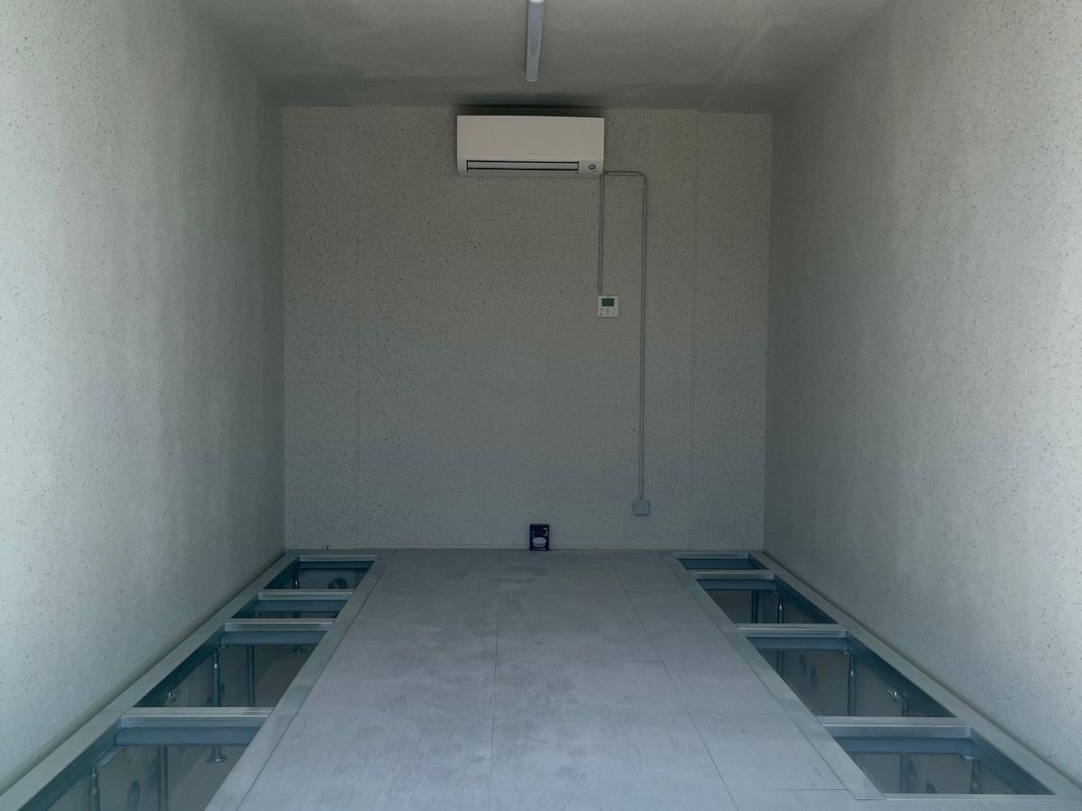 Interieur van een lege, rechthoekige ruimte met lichte muren en plafond. In het midden bevinden zich verzonken, glazen gedeeltes in de vloer.