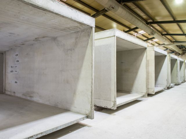 Rij betonnen elementen in een magazijninterieur, ruwbouw, zichtbare plafondinstallaties.