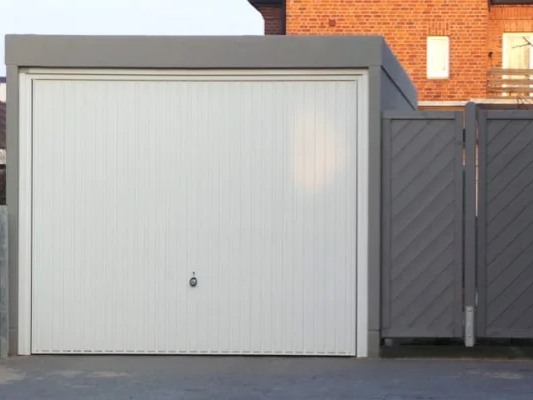 Een garage met witte roldeuren en grijze zijdeuren op een geplaveide oprit. Op de achtergrond een bakstenen huis.