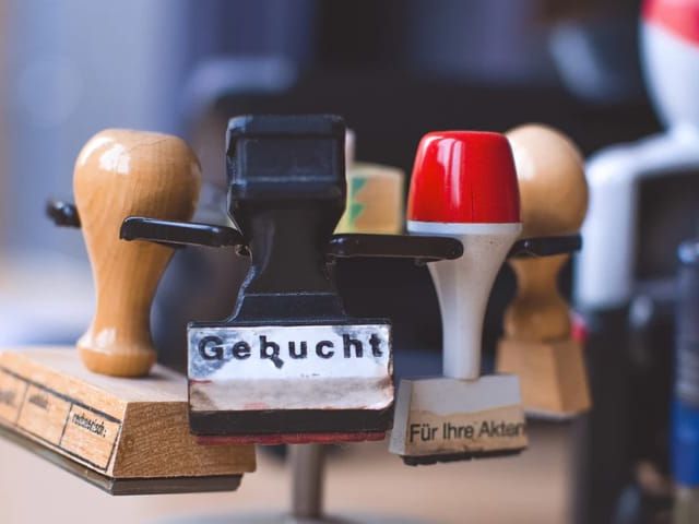 Verschillende stempels op elkaar gestapeld. Voorste stempel toont de tekst 'Gebucht'.