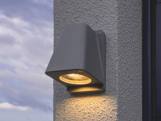 Wandlamp aan een gestucte gevel. Het licht schijnt warm naar beneden.