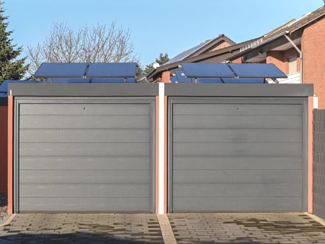 Dubbele garage met grijze sectionale deuren en zonnepanelen op het dak. Bestraatte oprit.