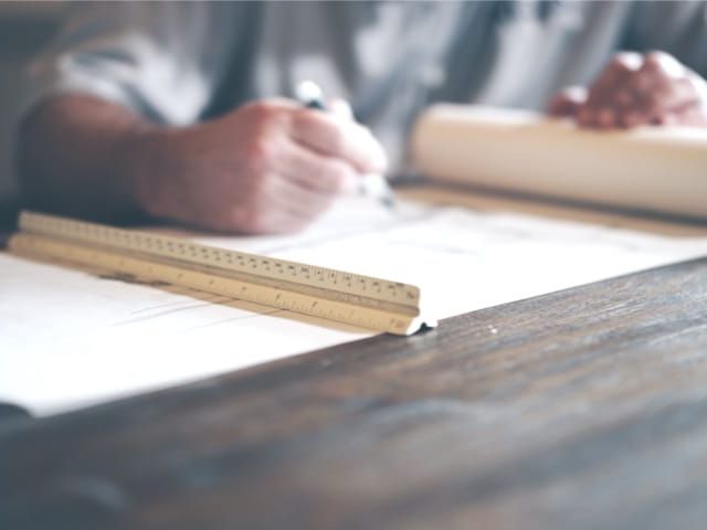 Architect aan het werk aan bouwtekeningen op een houten tafel. Lineaal op de tekeningen.