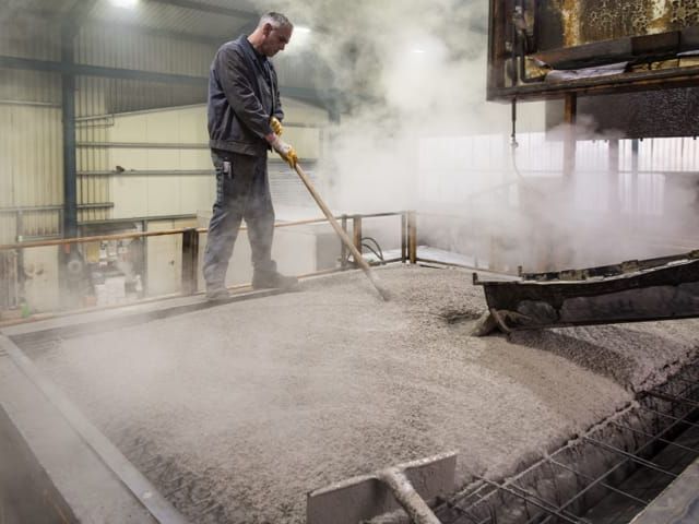 Arbeider in fabriekshal, verdeelt materiaal met hark over stoomende oppervlakte.