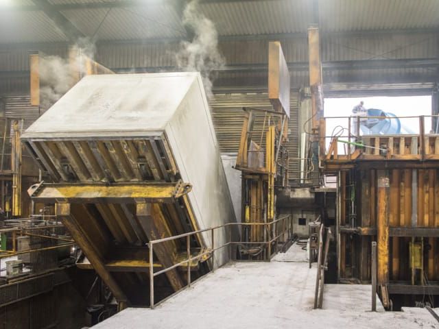 Industriehal met grote, schuine betonmal. Werknemers zichtbaar, er komt stoom vrij.