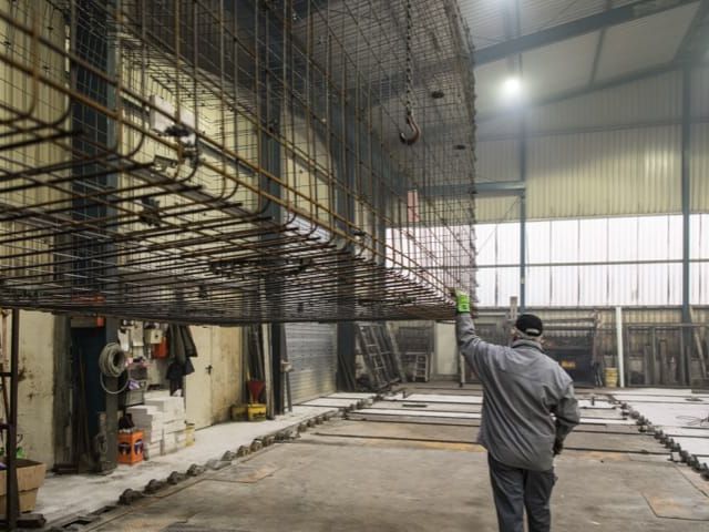 Hal met stalen wapening voor betonproducten. Arbeider met opgeheven hand inspecteert constructie.