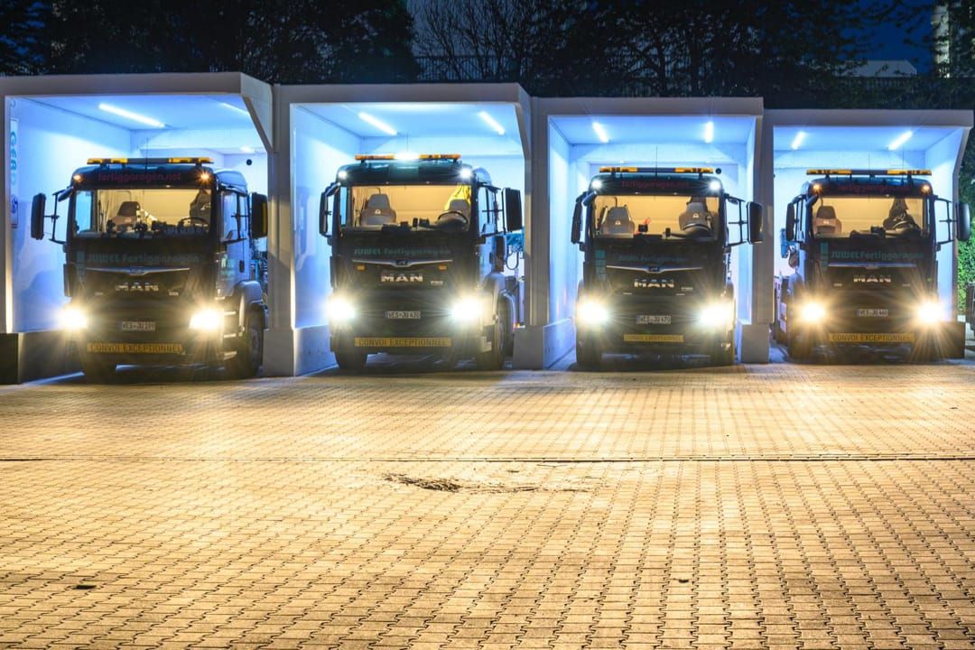 Sleutelklare JUWEL prefab garages bij nacht, vier verlichte garages met geparkeerde MAN-vrachtwagens, toont de snelle en eenvoudige installatie van betonnen prefab garages.