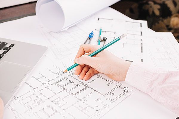 Architectenbureau: Hand tekent plattegrond met potlood op houten tafel, omringd door andere plattegronden en laptop.