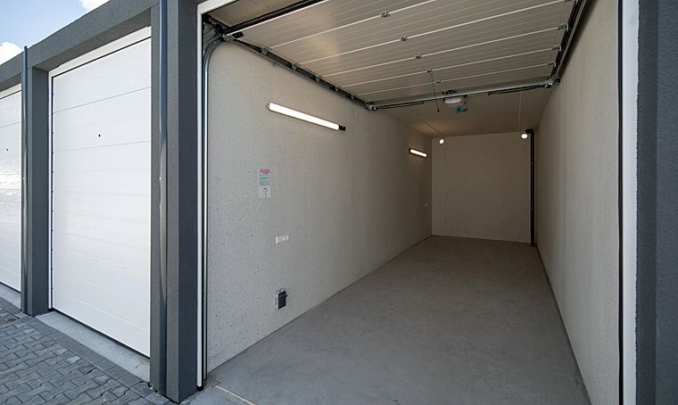 Lichte opslagruimte met open rolpoort. Binnenmuren en vloer zijn lichtgrijs. Verlichting aan het plafond.