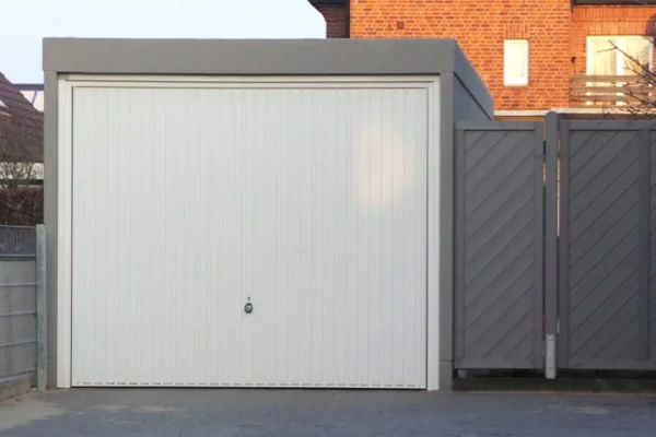 Een garage met witte roldeuren en grijze zijdeuren op een geplaveide oprit. Op de achtergrond een bakstenen huis.