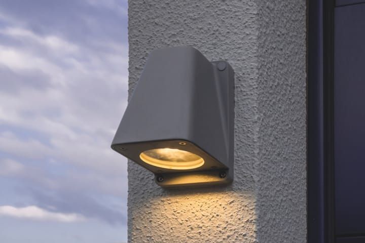 Wandlamp PYRA van zilverkleurig aluminium, gemonteerd op de buitenwand van een prefab garage, zorgt voor klassieke en efficiënte verlichting.