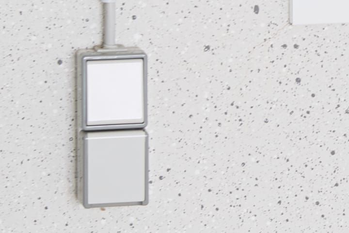 Een combinatie van lichtschakelaar en stopcontact in wit, onder elkaar gemonteerd, als opbouwvariant op een binnenwand van een garage